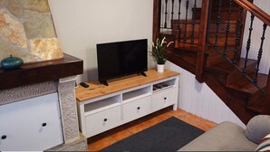 Una sala de estar con televisor sobre un mueble de madera, pared de piedra, escalera y sofá.