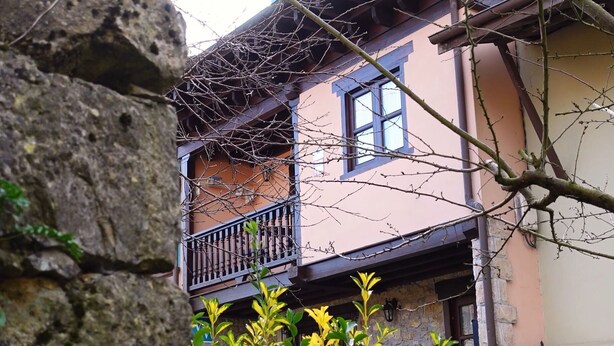 Un edificio de dos plantas con un balcón y un muro de piedra.