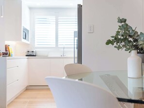 Une cuisine moderne avec des meubles blancs, une table en verre et une chaise blanche.