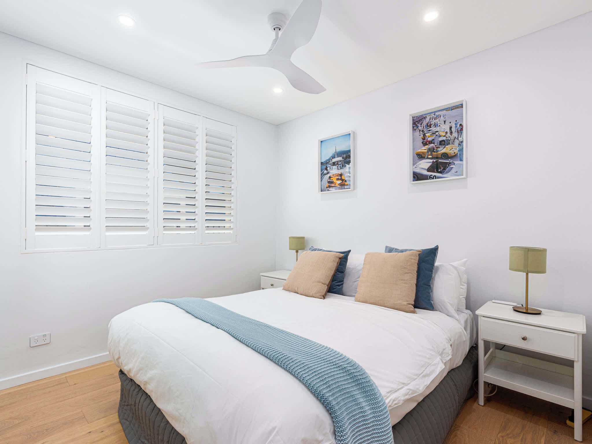 A bedroom with a bed, two bedside tables, a ceiling fan, and two wall-mounted pictures.