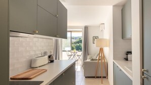 Eine moderne Küche mit grauen Schränken, einer weißen Arbeitsplatte und einem Holzschnittbrett. Es gibt einen Essbereich mit Tisch und Stühlen, sowie eine Lampe.