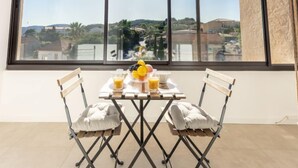 Ein Essbereich mit Tisch für zwei Personen, Blick auf eine Stadtlandschaft durch große Fenster und ein kleiner Balkon mit Aussicht.