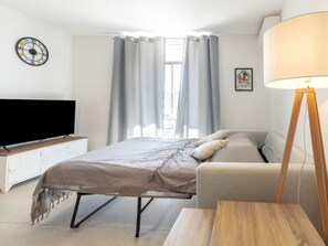 Une chambre moderne avec un lit, une table de chevet, une télévision, des rideaux et une lampe.