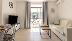 Ein modernes Wohnzimmer mit Flachbildfernseher, einem Esstisch mit Stühlen, einer Couch und einem Balkon mit Tisch und Stühlen.
