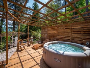 Een hottub onder een houten pergola met stoelen, omringd door een houten terras en een stenen muur.