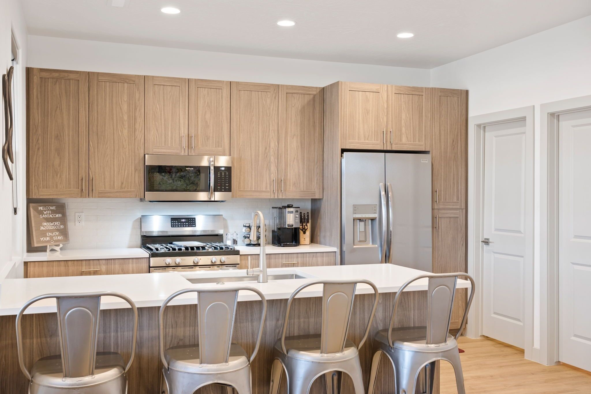 Una cocina moderna con armarios de madera, electrodomésticos de acero inoxidable y una isla central con taburetes de bar.
