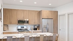 A modern kitchen with wooden cabinets, stainless steel appliances, and a central island with bar stools. - Santa Clara Comfort #39 by RedAwning (Santa Clara)