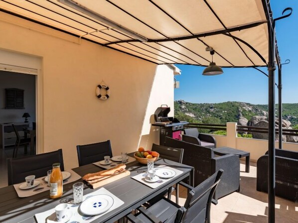 A dining area with a table set for two, a grill, and a view of the landscape.