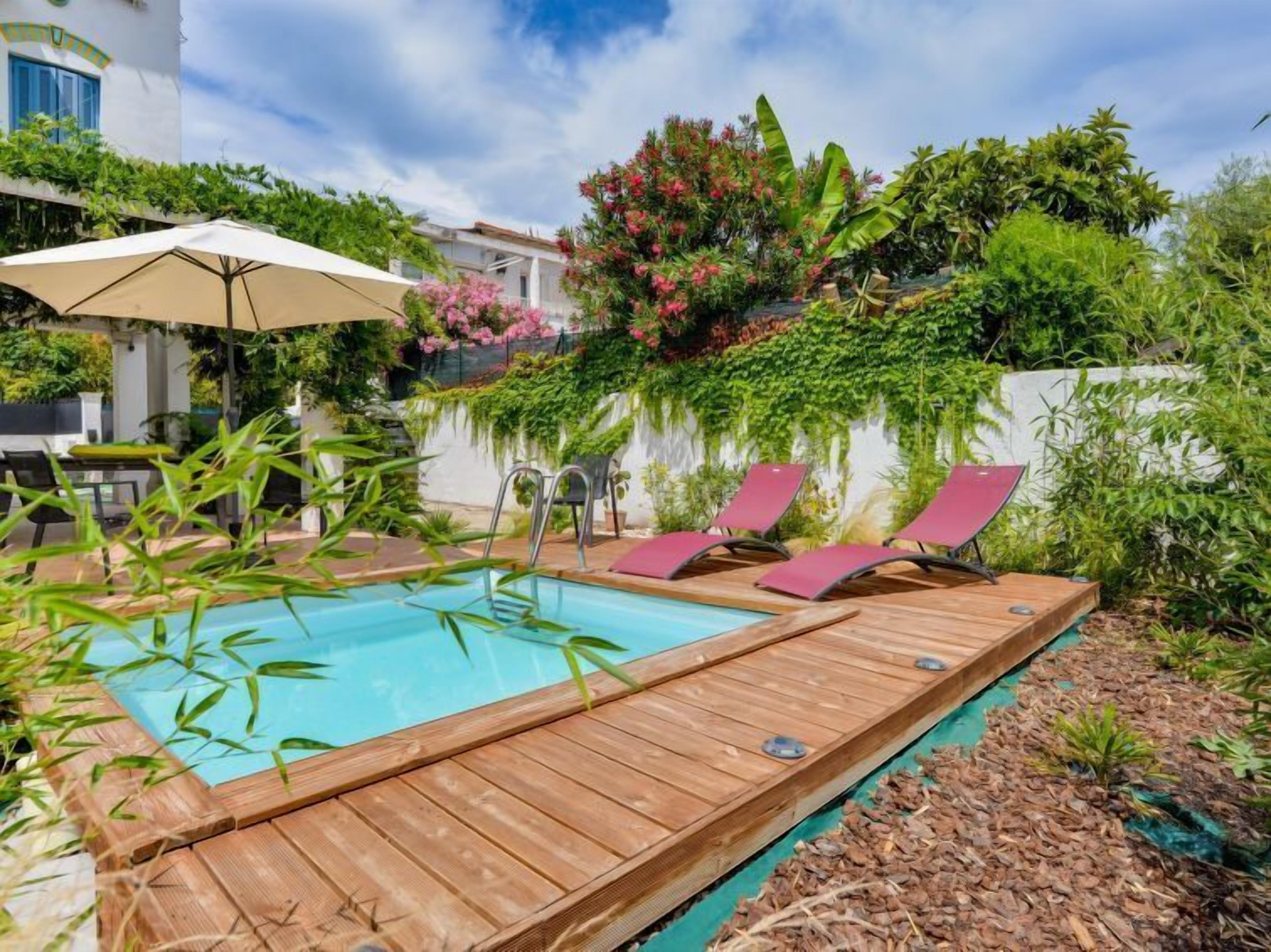 Un terrazzo in legno con piscina, sedie a sdraio e un tavolo sotto un ombrellone.