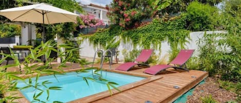 Un terrazzo in legno con piscina, sedie a sdraio e un tavolo sotto un ombrellone.