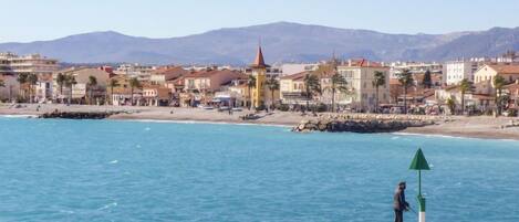 A coastal town with a rocky shoreline, a lighthouse, and buildings with red roofs.