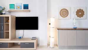 Un soggiorno moderno con una televisione a schermo piatto montata a parete, un mobile basso in legno con cassetti, un tavolino con un vaso e decorazioni murali.