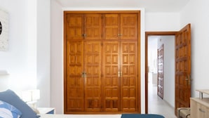 Una camera da letto con un ampio armadio in legno, un letto con copriletto blu e bianco e un comodino in legno.