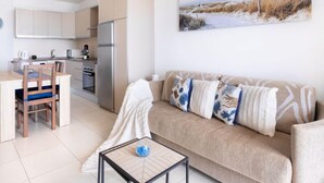 Un appartamento moderno con angolo cottura, un divano con cuscini decorati e un quadro raffigurante una spiaggia.