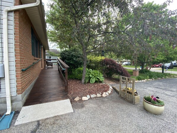 A covered outdoor area with a wooden deck, a brick building, and a garden with various plants and a wooden fence. - Suite Springs (Yellow Springs)