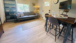 A cozy living space with a sofa, a dining table with chairs, a ceiling fan, a clock, and a TV mounted on the wall. - Suite Springs (Yellow Springs)