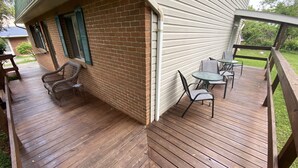 A wooden deck with outdoor furniture, a brick wall, and a white siding house. - Suite Springs (Yellow Springs)