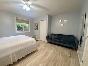 A bedroom with a bed, a blue sofa, a small table, and a door.
