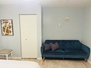 A room with a bed, a blue sofa, a white door, and a wall with three round mirrors.