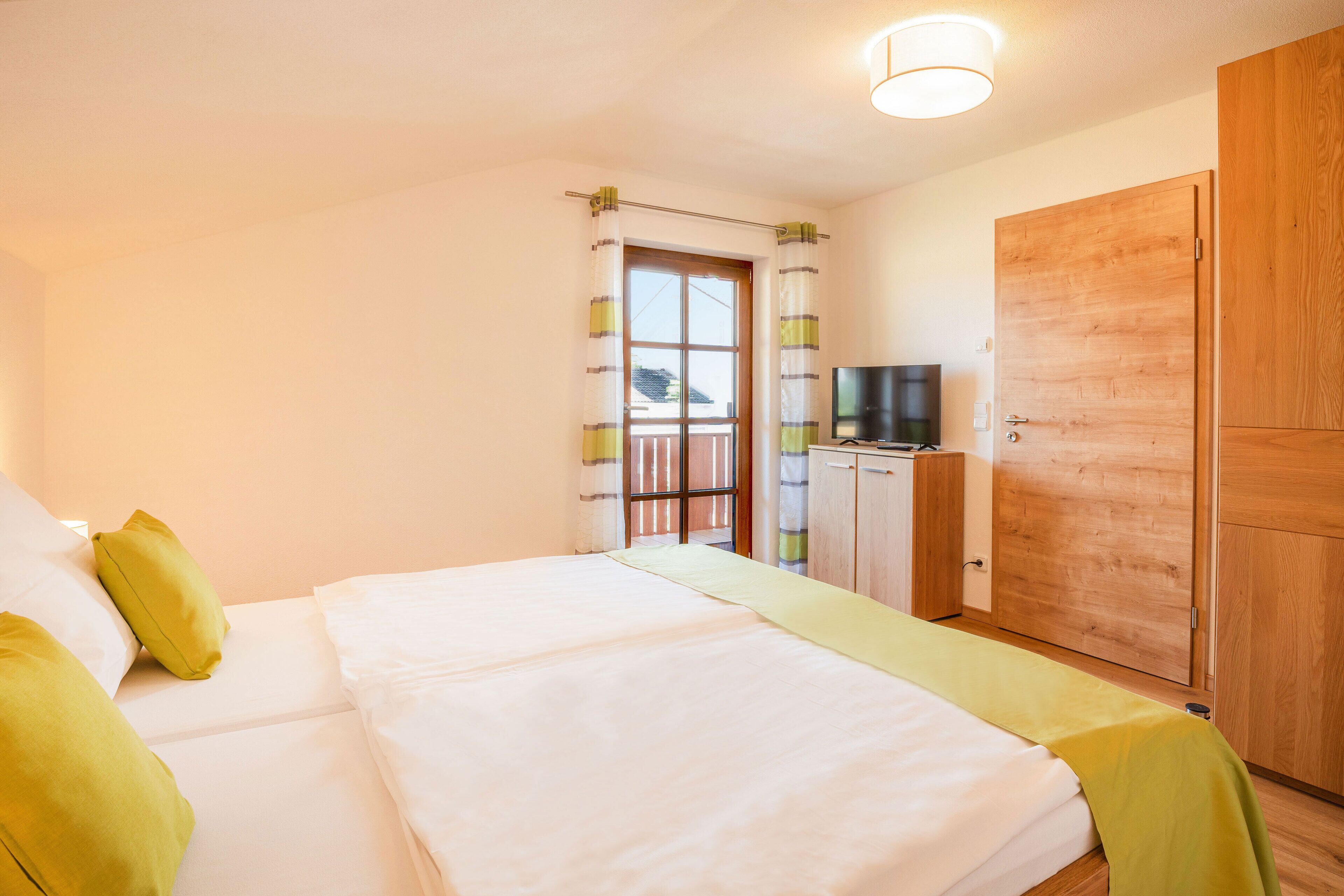 Un dormitorio con cama, televisor, armario y ventana con cortinas.