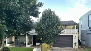 A modern two-story house with a black garage door, a visible mailbox, and a well-maintained lawn. - Fi's Beach Pad (Port Macquarie)