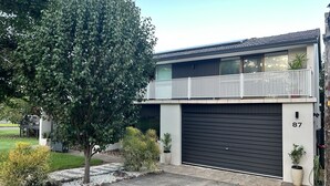 A modern two-story house with a garage, a balcony, and a large tree in the front yard. - Fi's Beach Pad (Port Macquarie)