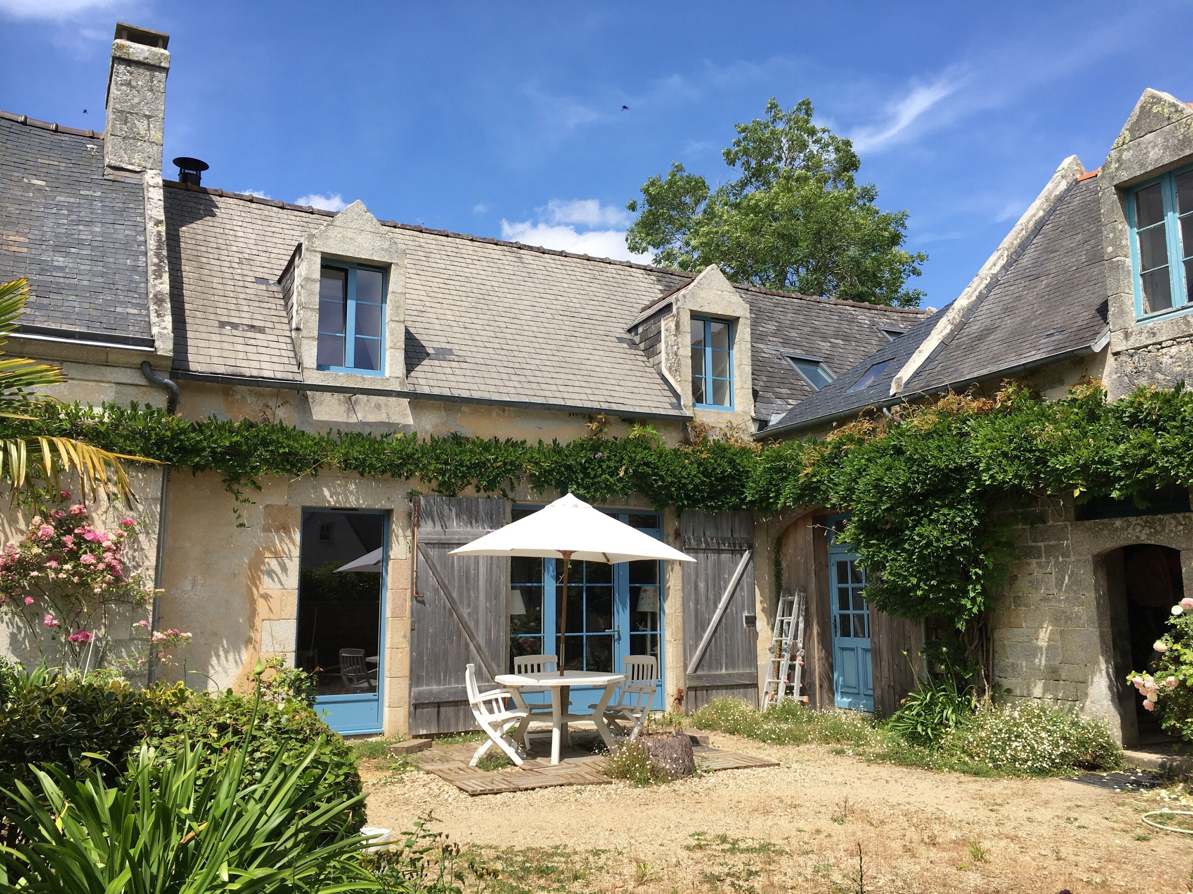 Ein traditionelles Steinhaus mit einer Veranda, einem Tisch mit Stühlen und einer an der Wand angelehnten Leiter.