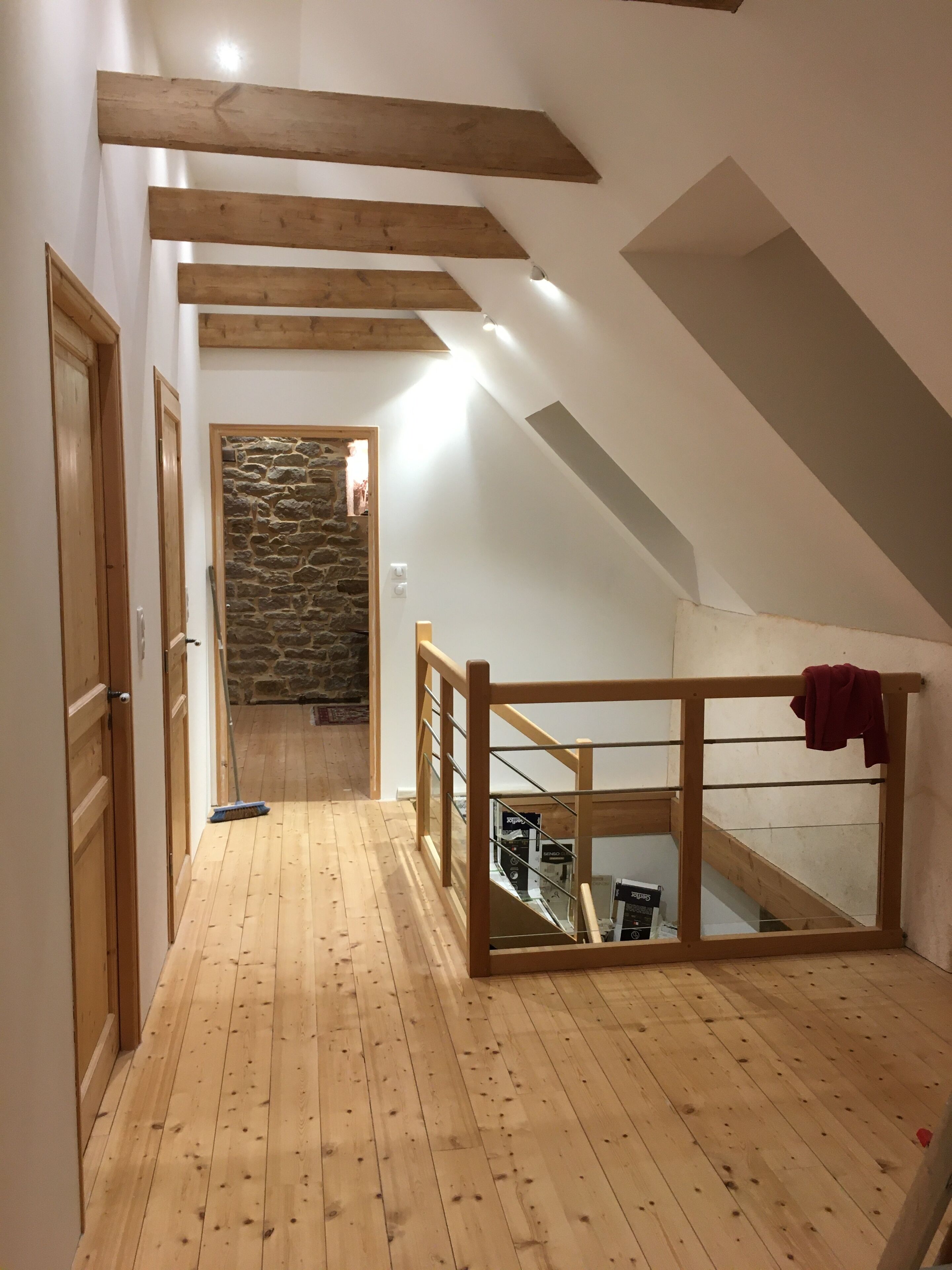 A wooden staircase with a glass balustrade leading to a loft area with a stone wall and a red towel hanging on the railing.