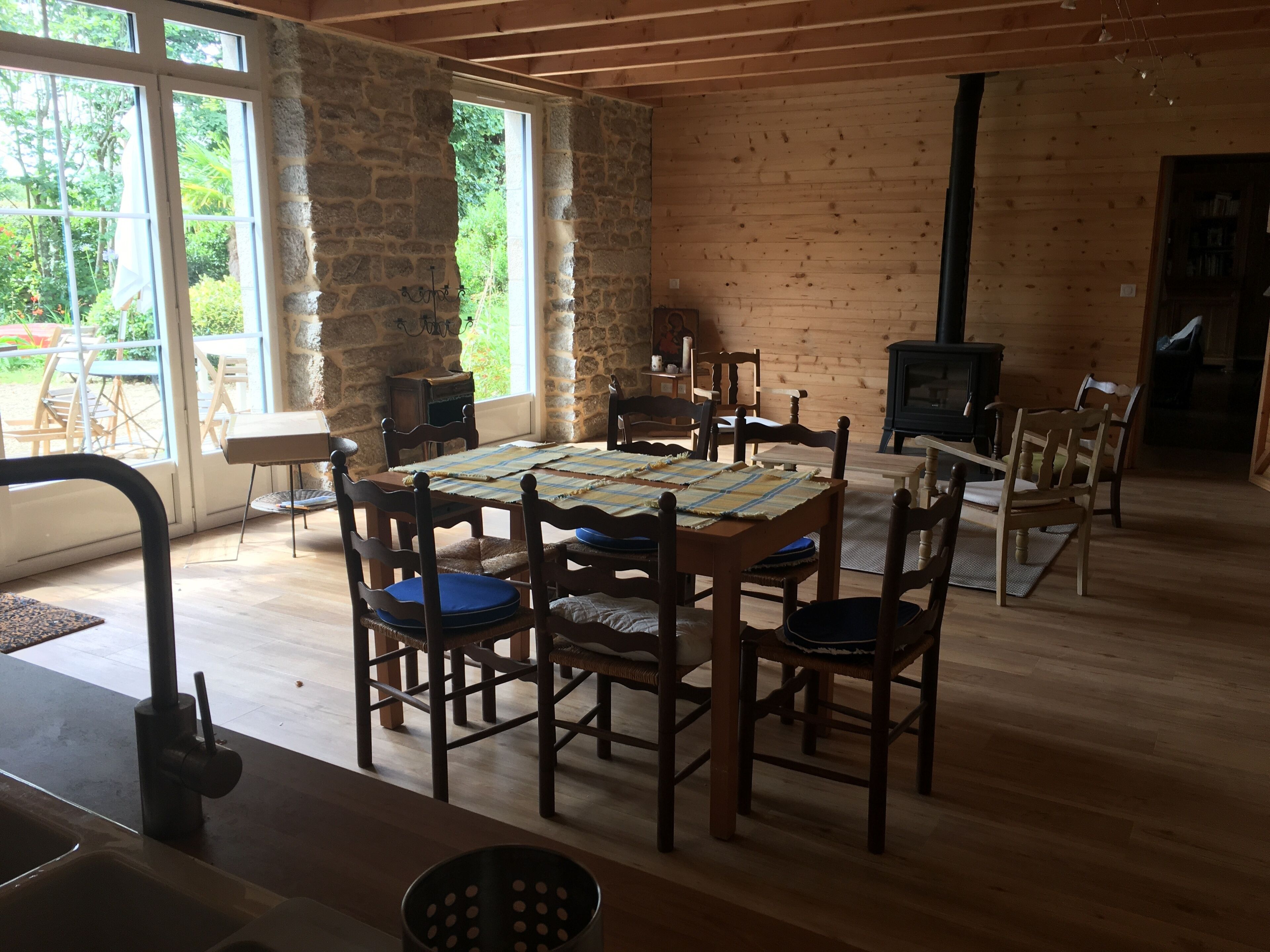 Un intérieur en bois avec un mur en pierre, une table à manger avec des chaises, une cheminée et une vue dégagée sur l’extérieur grâce à de grandes fenêtres.
