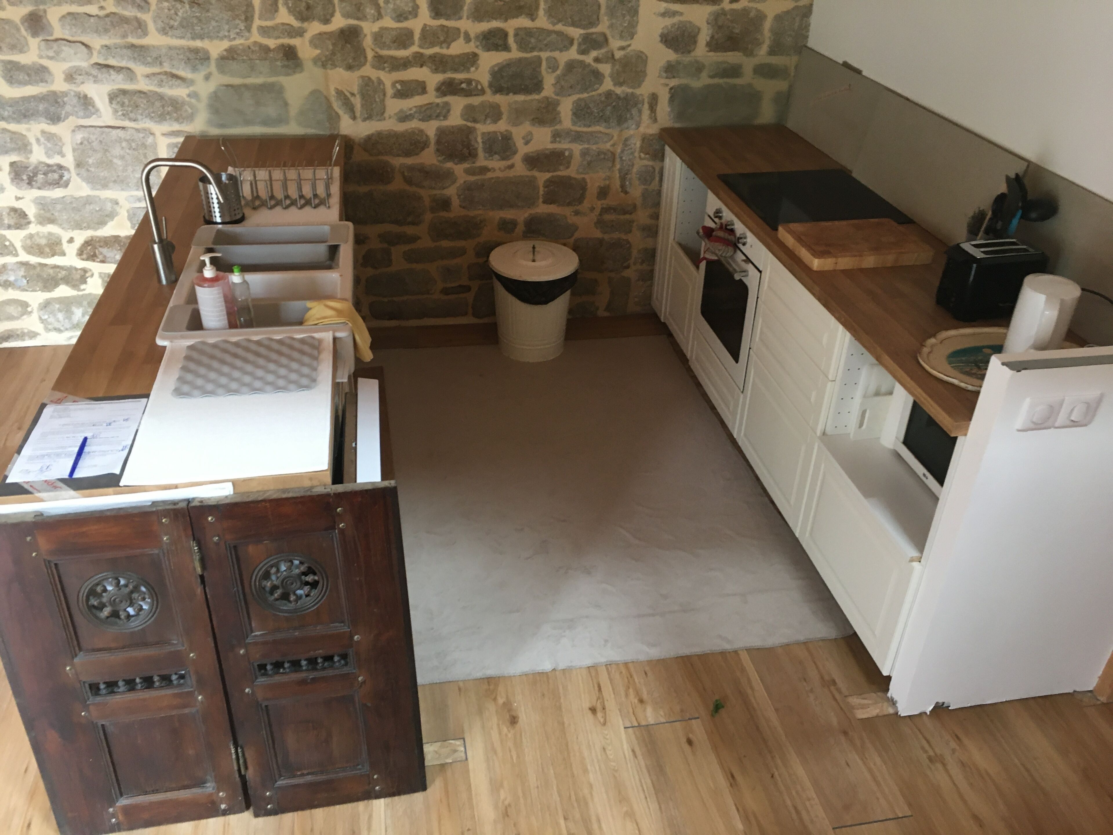 A compact kitchen with a stone wall, wooden countertop, and white appliances.