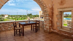 A stone-walled room with a table and chairs, a window overlooking a pool and greenery. - Independed Stone villa common pool (Παλαιλώνι)