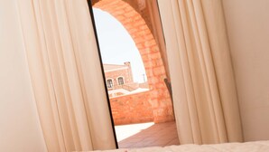 A bed with a single red rose, beige curtains, and a view of a brick building through an arched window. - Independed Stone villa common pool (Παλαιλώνι)