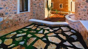 A courtyard with stone flooring, a small garden, and buildings with stone walls and windows. - Independed Stone villa common pool (Παλαιλώνι)