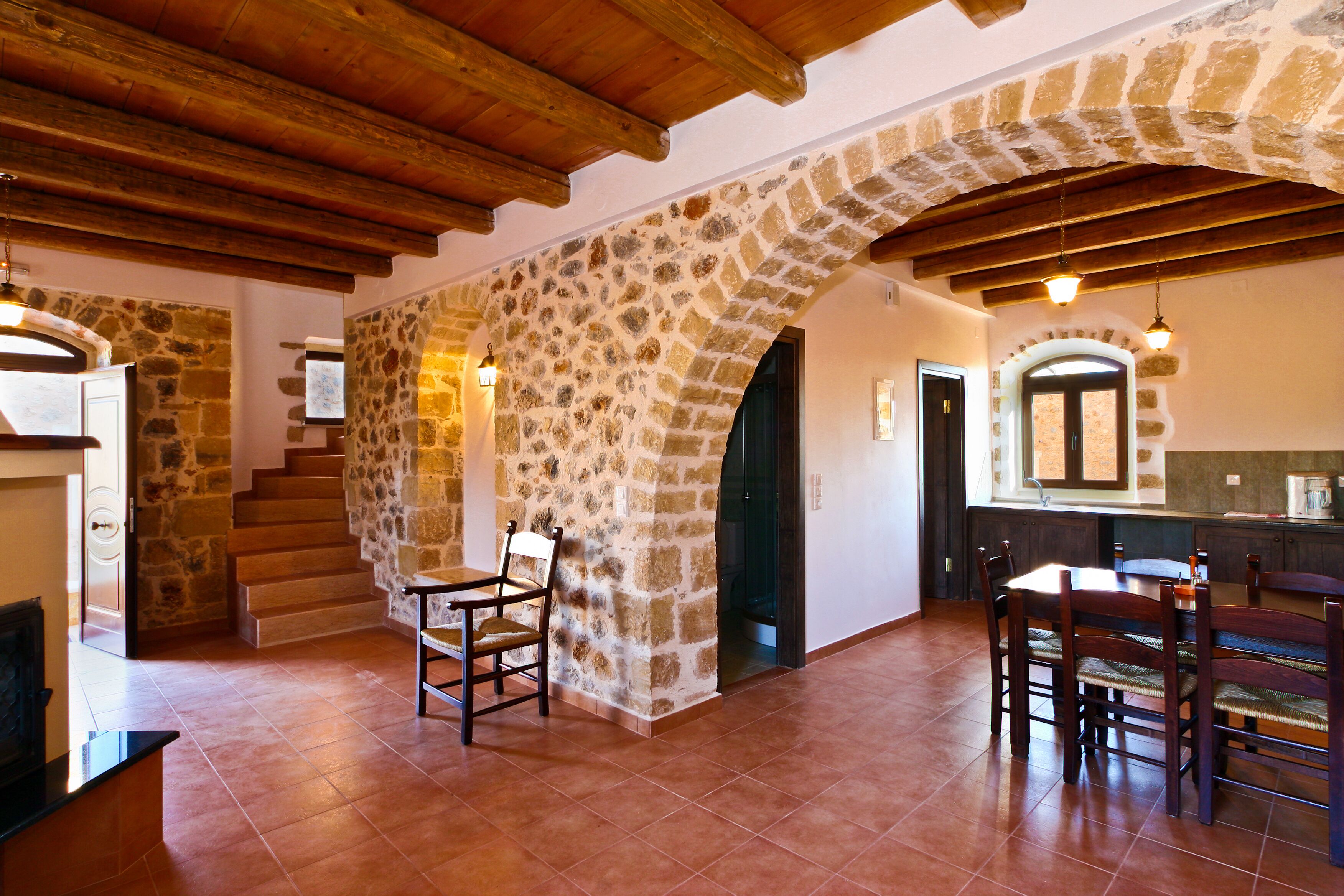A spacious kitchen with stone walls, wooden beams, and a dining area with chairs and a table.