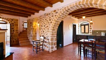 A spacious kitchen with stone walls, wooden beams, and a dining area with chairs and a table.