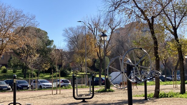 Um parque com equipamentos de ginástica, árvores e carros estacionados.