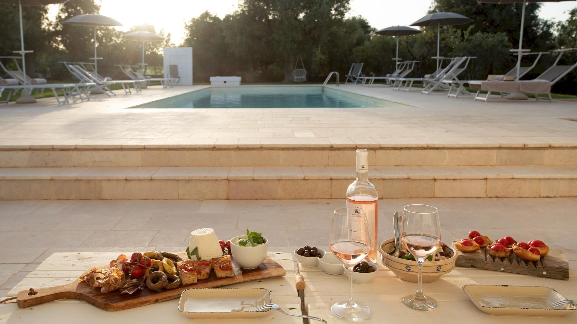 An outdoor dining area with a pool, lounge chairs, and a table set with food and drinks.