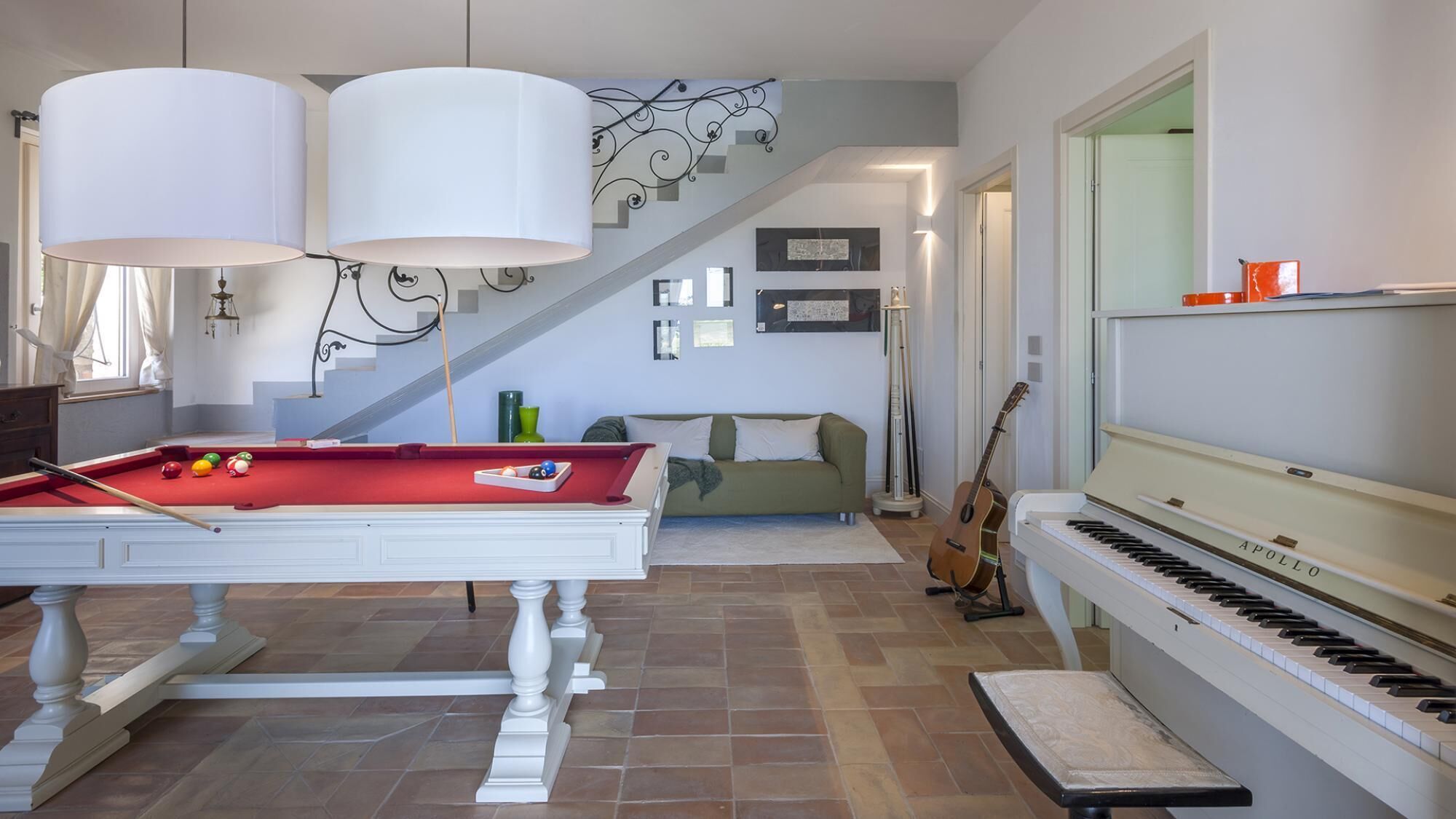 Una habitación con mesa de billar, piano, escalera y sofá.