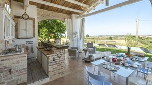 A rustic kitchen with a brick stove, white cabinets, and a dining area with a table set for breakfast. - Casa Pilar 4 1 in Staffolo (Staffolo)