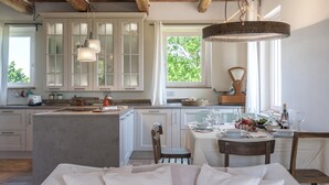 A modern kitchen with a central island, white cabinetry, and a large window providing natural light. - Casa Pilar 4 1 in Staffolo (Staffolo)