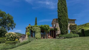 A stone building with a steep roof, surrounded by lush greenery and a well-maintained lawn. - Casal Parro 6 in Perugia (Perugia)