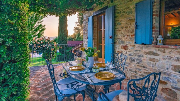 An outdoor dining area with a stone wall, blue shutters, and a table set for two with chairs. - Casal Parro 6 in Perugia (Perugia)