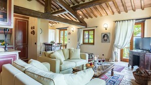 A cozy living room with a sofa, a coffee table with drinks, and a TV. There's a dining area with a table and chairs, and a kitchen with cabinets and a sink. - Casal Parro 6 in Perugia (Perugia)