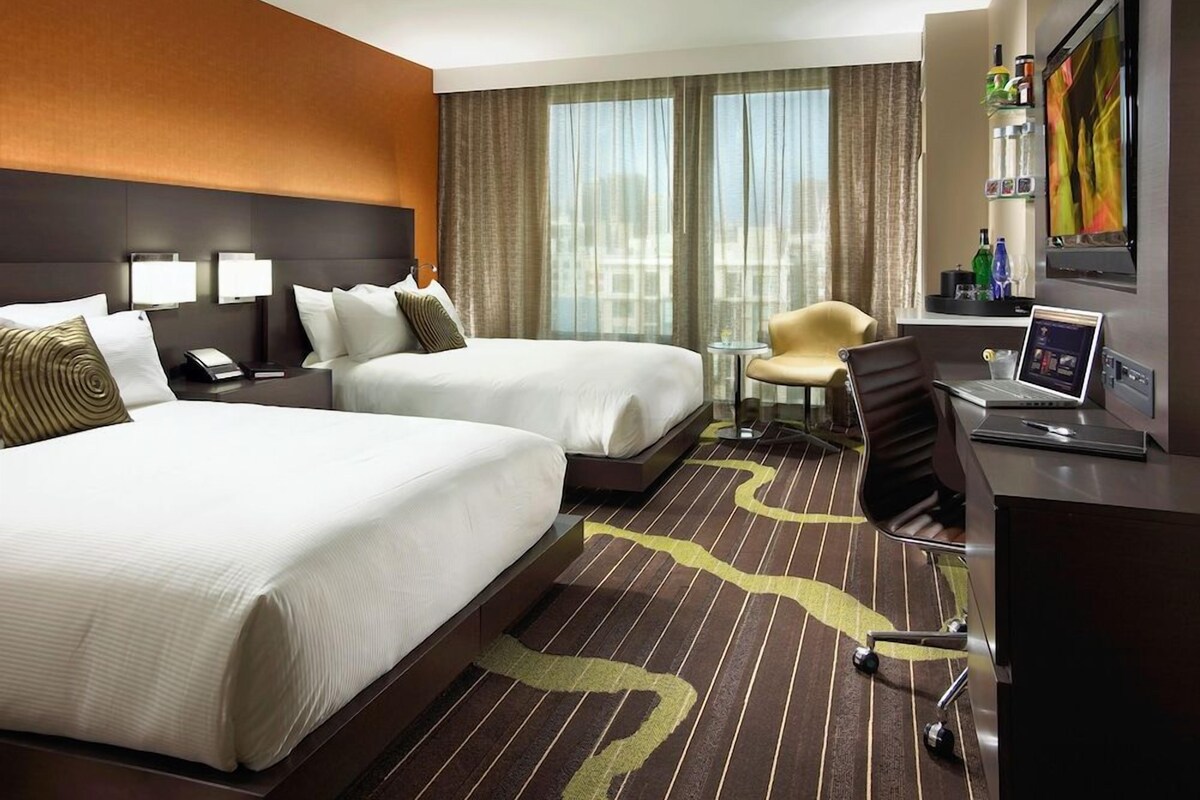 Een hotelkamer met twee bedden, een bureau, een stoel, een televisie en een raam met gordijnen.