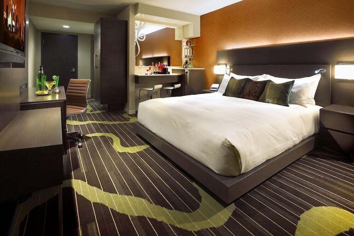 Una habitación de hotel con cama, escritorio, silla, espejo y minibar.