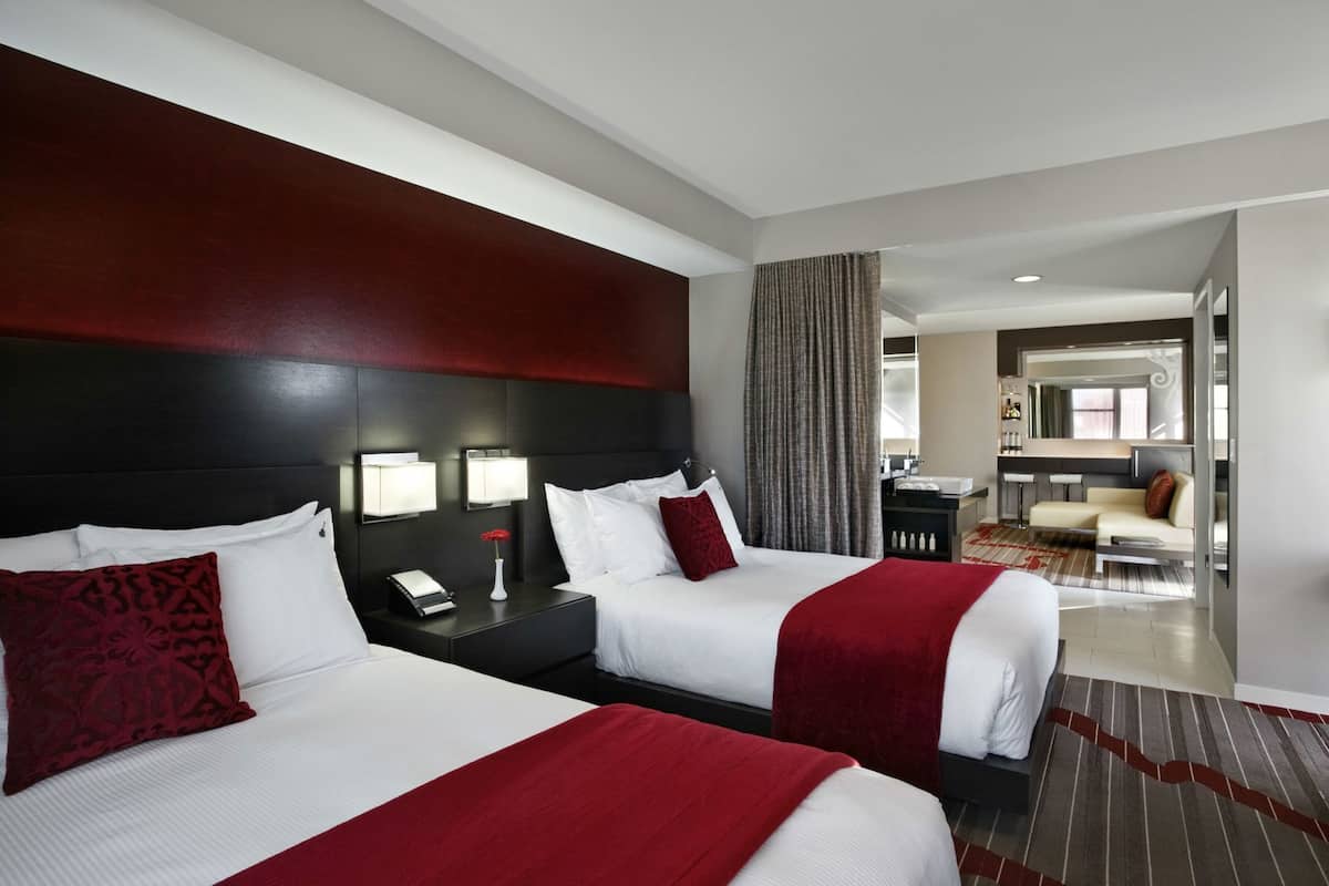 Habitación de hotel con dos camas, un escritorio, una silla y un baño visible a través de una puerta abierta.