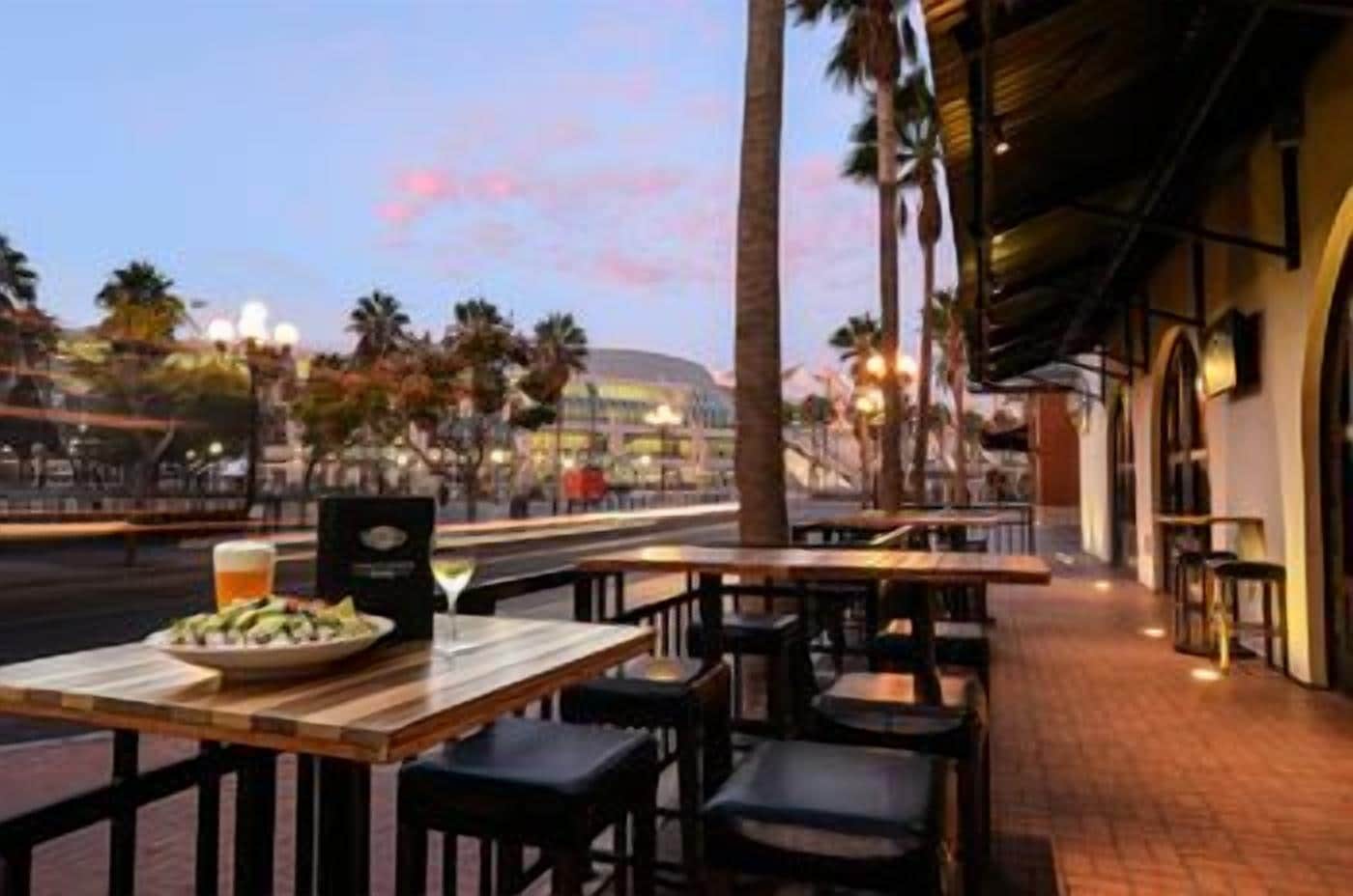 An outdoor dining area with tables and chairs, a view of the cityscape, and palm trees.