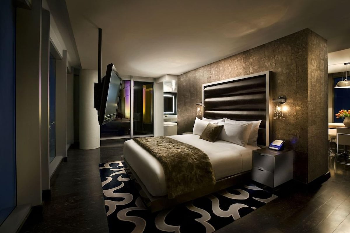 Een moderne hotelkamer met een groot bed, een nachtkastje, een aan de muur bevestigde televisie en een badkamer die door een open deur zichtbaar is.