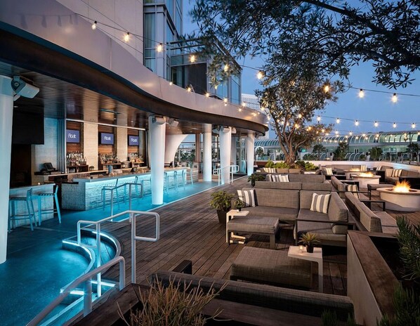 Un bar en la azotea con piscina, asientos exteriores y luces colgantes.