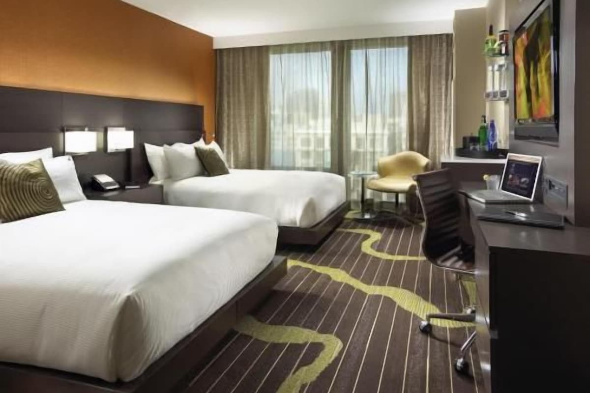 Een hotelkamer met twee bedden, een bureau, een stoel en uitzicht op de stad.